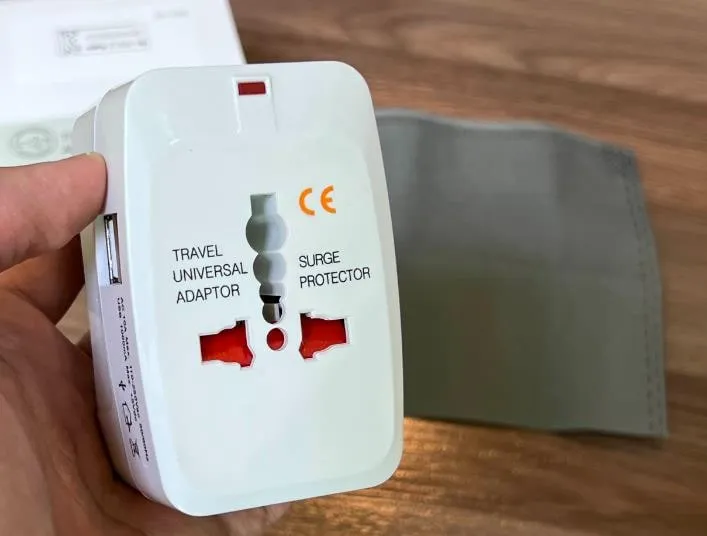 어댑터 앞면. TRAVEL UNIVERSAL ADAPTOR, SURGE PROTECTOR 글자와 주황색 CE 마크, 여러 모양이 겹친 만능 콘센트 구멍