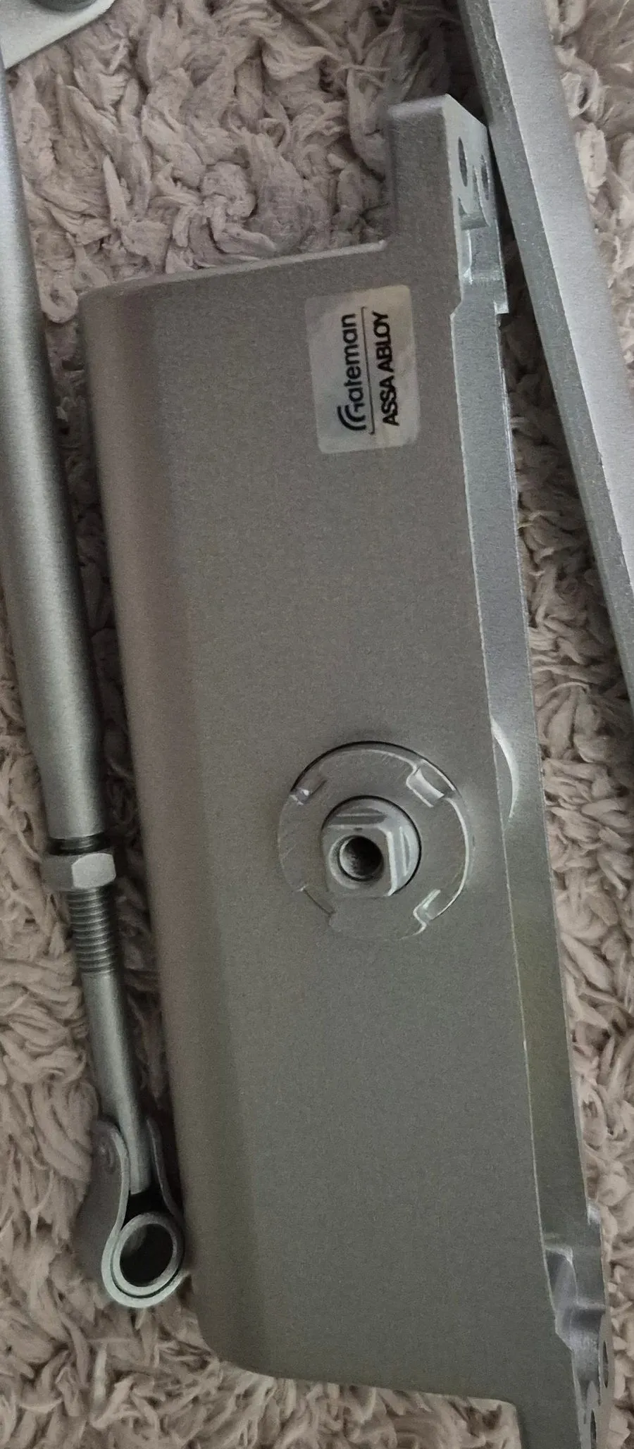 도어클로저 본체 근접. Gateman ASSA ABLOY 스티커와 가운데 축 구멍