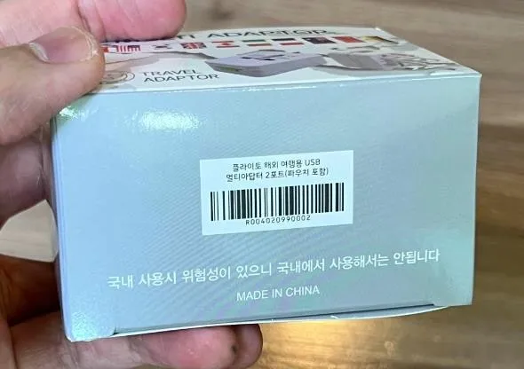 상자 옆면 라벨. 플라이토 해외 여행용 USB 멀티아답터 2포트(파우치 포함) 표기와 바코드, 그 아래 국내 사용 금지 문구