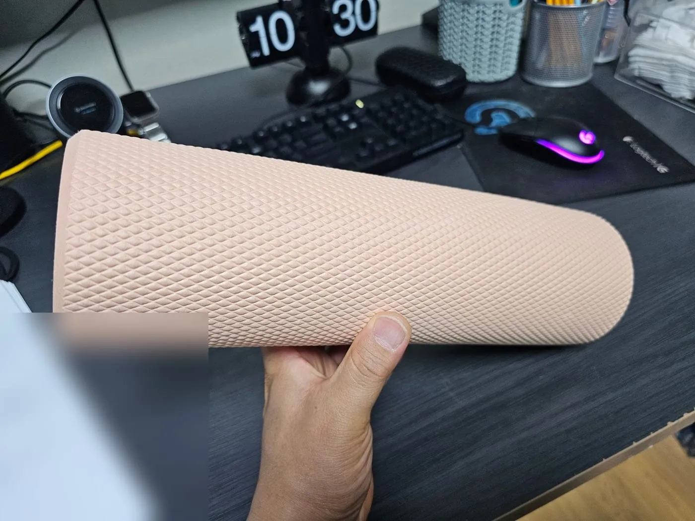 한 손으로 폼롤러를 받쳐 든 모습. 키보드가 있는 책상 위다