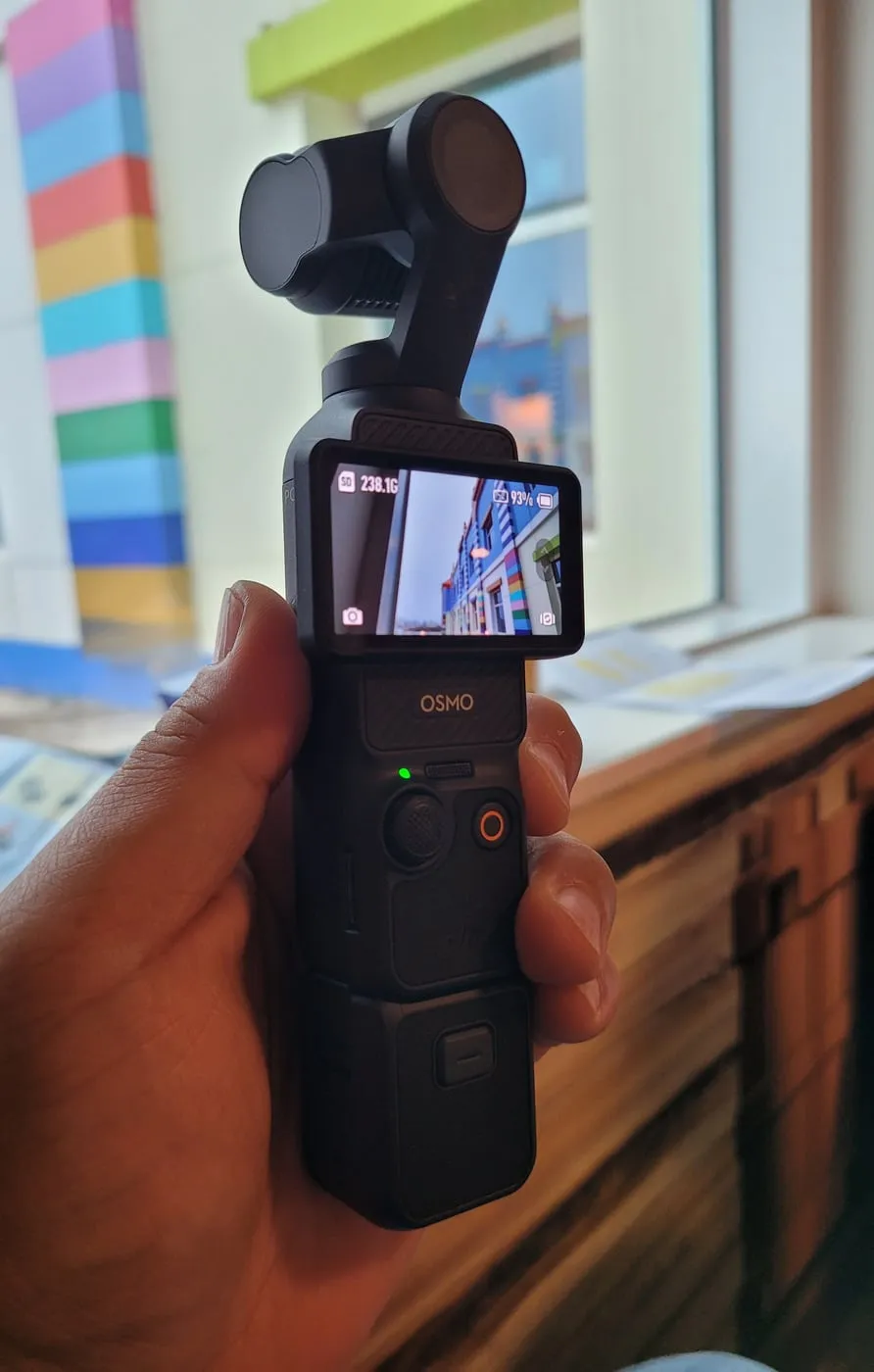 한 손에 쥔 DJI 오즈모 포켓3. 위쪽에 짐벌 카메라 헤드, 아래에 화면과 버튼