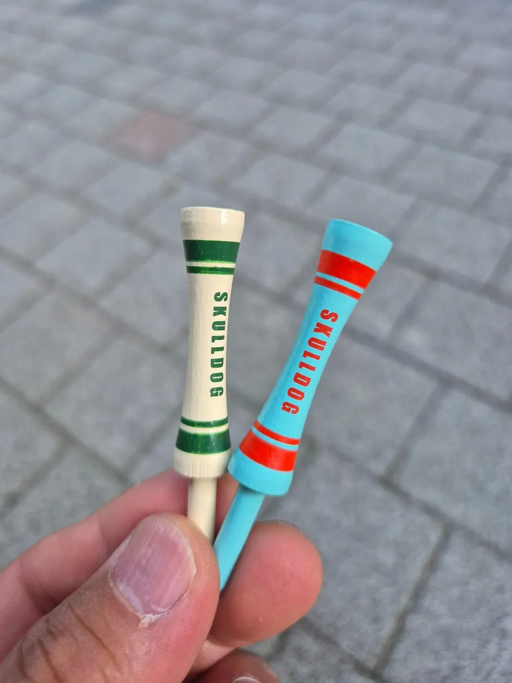세워서 잡은 두 티의 윗부분. 컵 모양 머리 아래에 굵은 띠와 가는 띠가 한 쌍씩 들어가 있고 SKULLDOG 글자가 세로로 찍혀 있다