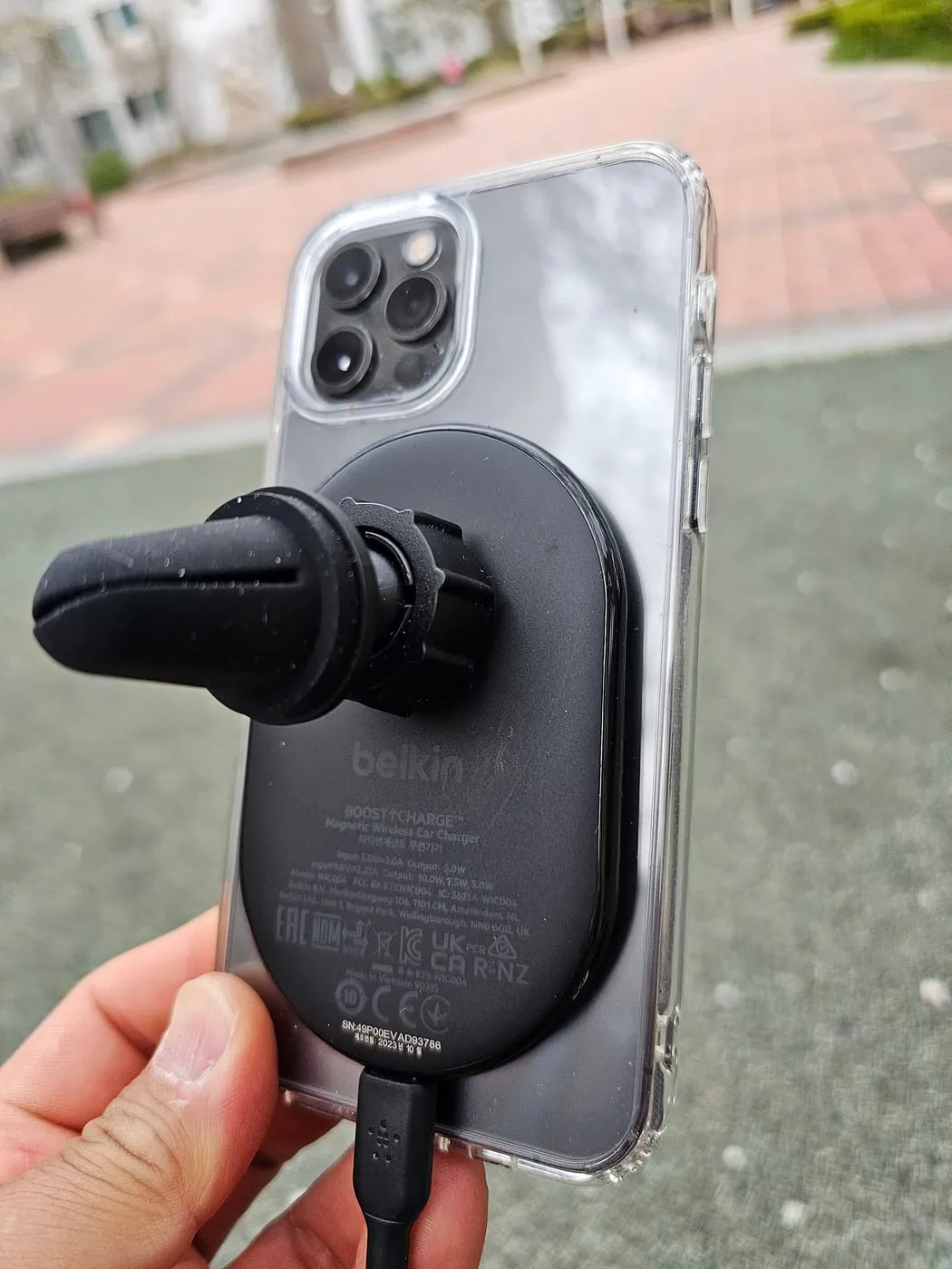 An iPhone in a clear case attached magnetically to the charger, held in one hand