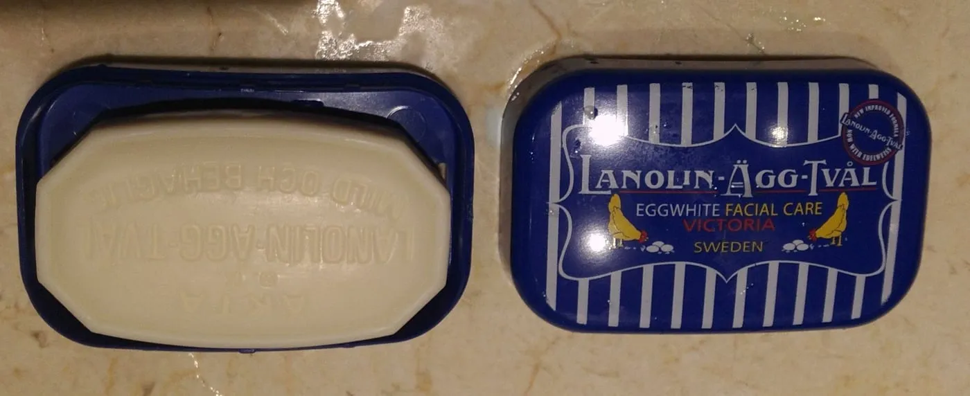 틴 비누케이스를 연 모습. 왼쪽에 흰 비누 한 개, 오른쪽 뚜껑에 LANOLIN-ÄGG-TVÅL 파란 줄무늬 디자인