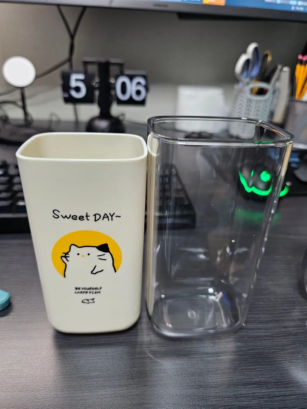 아이보리 컵과 투명 컵을 나란히 놓은 모습. 아이보리 컵에는 Sweet DAY와 고양이 그림이 있다