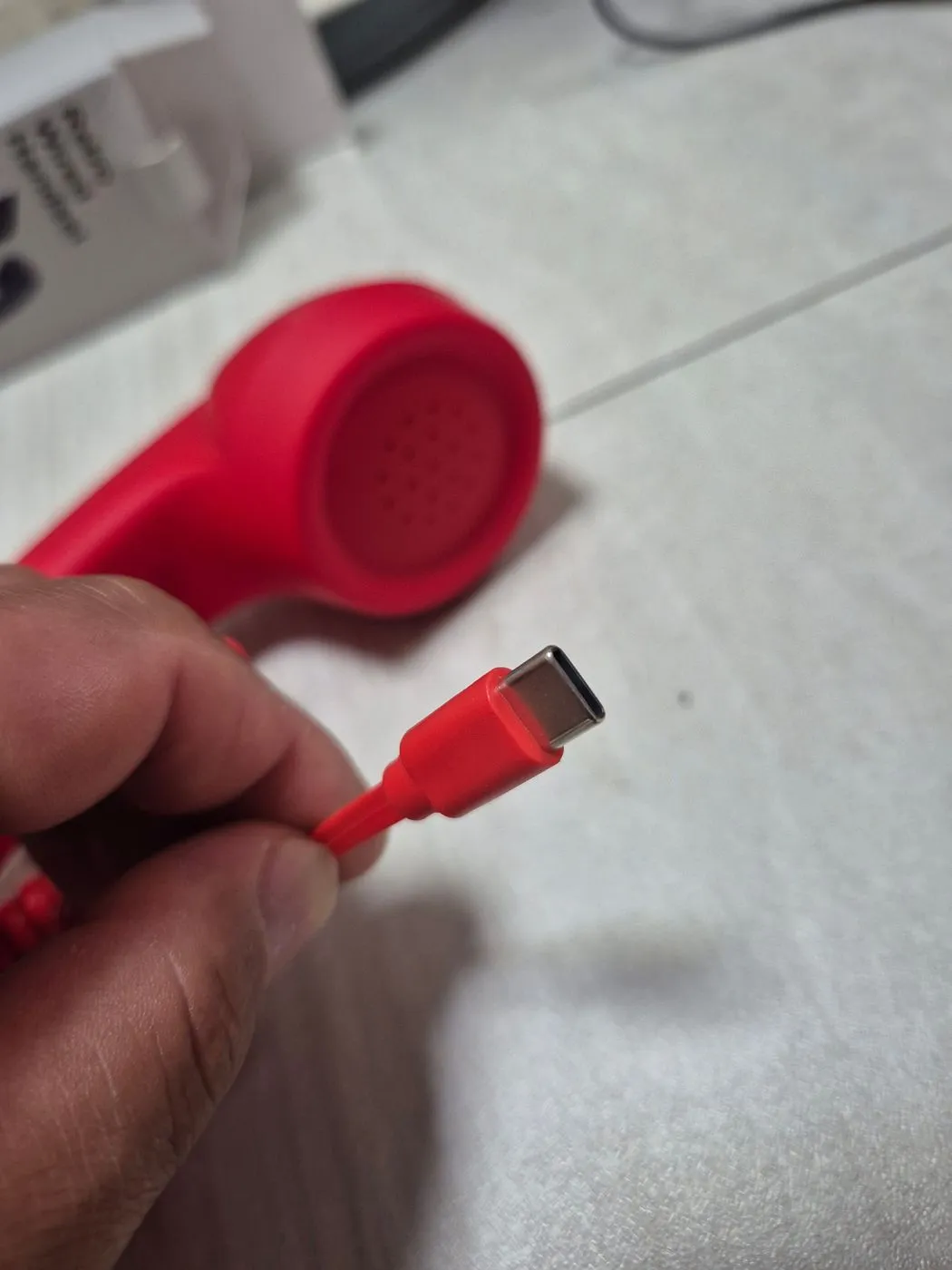손가락으로 집은 빨간 USB-C 단자. 뒤로 수화기가 보인다